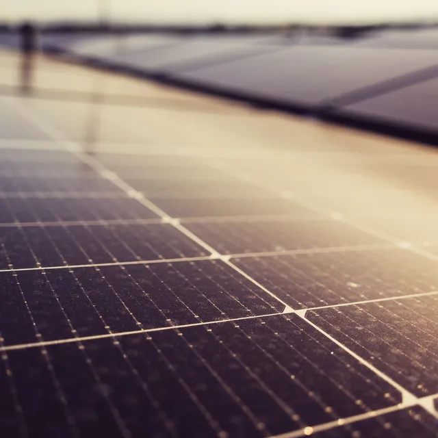 Hilera de módulos fotovoltaicos oscuros con el sol bajo reflejado en la superficie